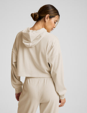 Woman wearing a beige cropped hoodie and pants on a light gray background. 