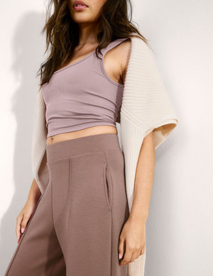 Woman wearing a pink ribbed cropped tank and brown pants against a plain background. 