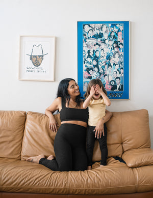A toddler in black Spacedye Toddler Legging plays on a tan couch with a woman in matching Darkest Night marled activewear.
