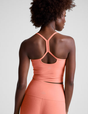 Woman wearing a peach-colored cropped tank and leggings on a plain background. 