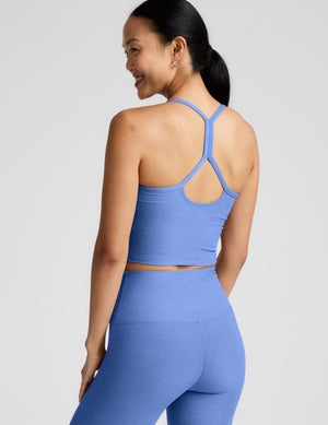 Woman wearing a blue cropped tank and leggings against a light gray background. 