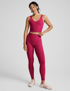 Woman wearing a red cropped v-neck tank and leggings against a plain background. 