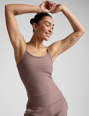 Woman wearing a brown tank top and pants against a plain background. 