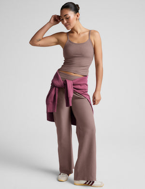 Woman wearing a brown tank top and pants against a plain background. 