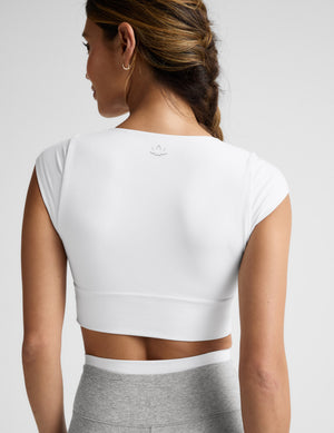 Woman wearing a white crop top and gray pants on a light background. 