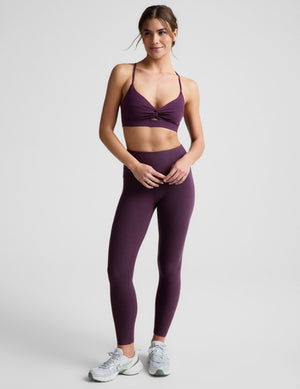 Woman wearing a purple sports bra and leggings on a light gray background. 
