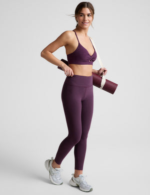 Woman wearing a purple sports bra and leggings on a light gray background. 