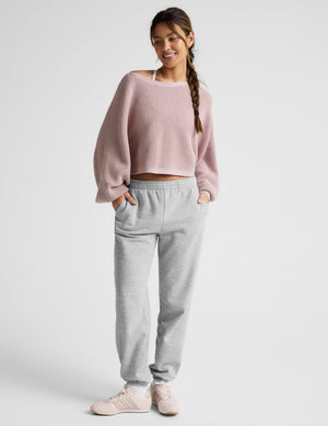 Woman wearing a pink sweater and gray sweatpants on a white background. 