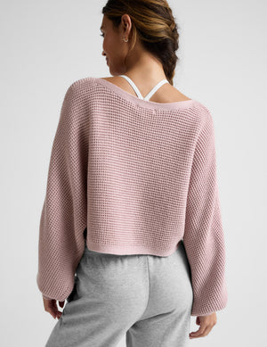 Person wearing a pink waffle sweater and gray pants on a white background. 