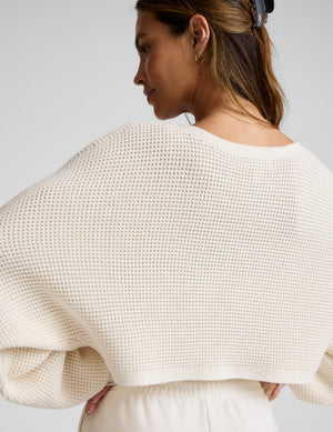Woman wearing a white textured sweater against a plain background. 