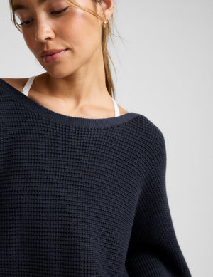 Woman wearing a navy sweater and shorts on a white background. 